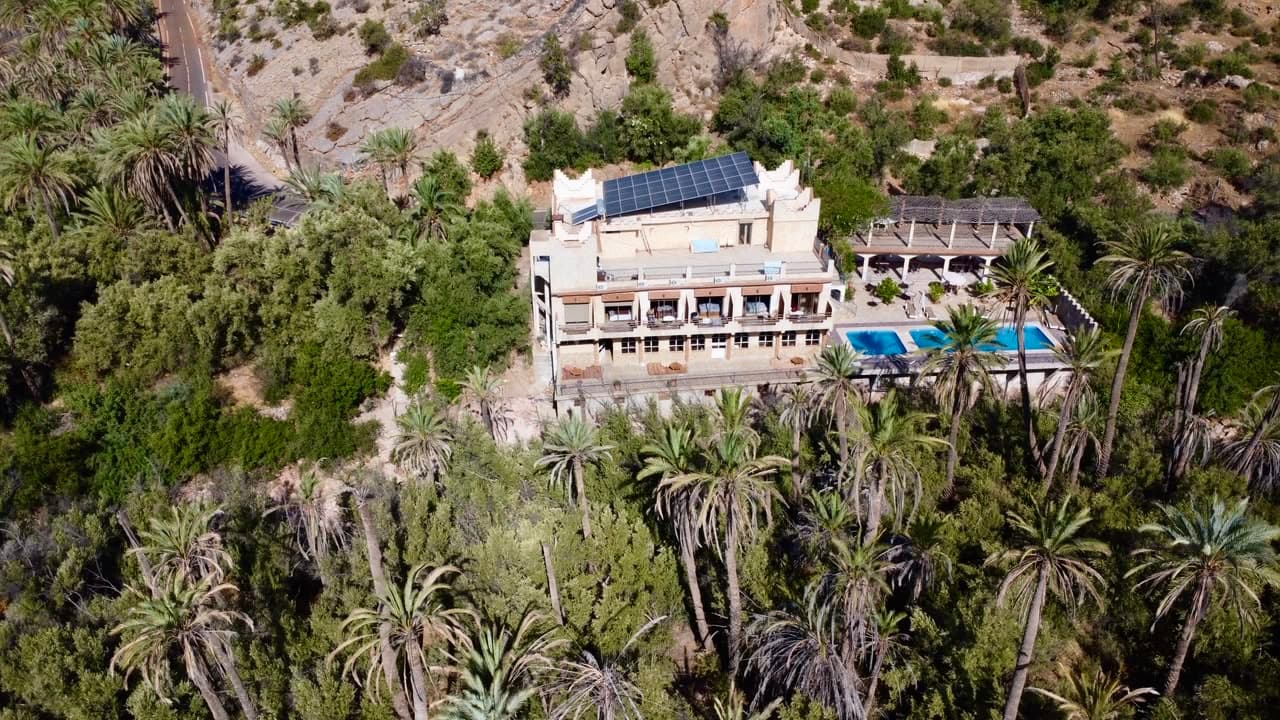 An aerial view of a building surrounded by a dense palm valley and mountains