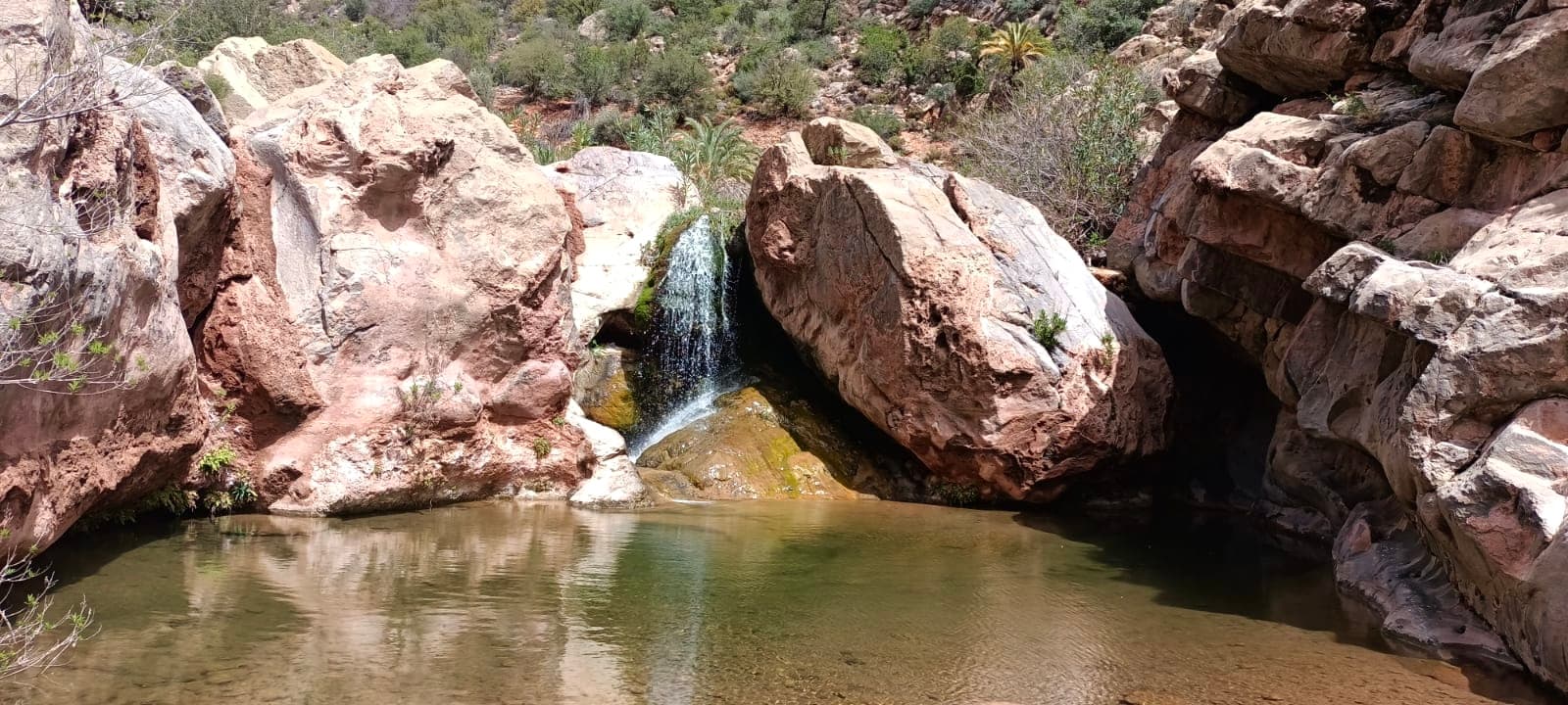 A small waterfall flowing between large boulders into a calm natural pool
