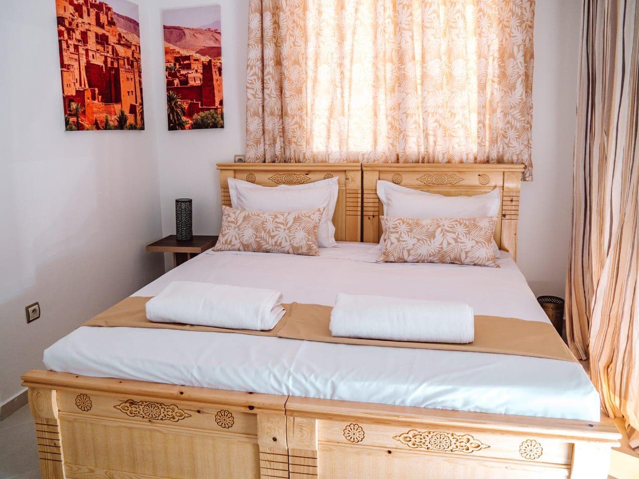 A sunlit bedroom with warm wood furniture and framed photographs of Moroccan kasbahs